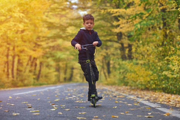 Cute boy riding scooter, outdoor in autumn environment on sunset warm light