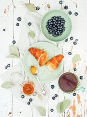 Top view of fresh croissants served with ripe blueberries and apricot jam  with tea on green plate over shabby background © PINKASEVICH