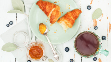 Top view of fresh croissants served with ripe blueberries and apricot jam  with tea on green plate over shabby background © PINKASEVICH