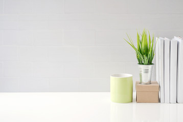 Mock up green mug, paper box, houseplant and books on white table with white brick wall