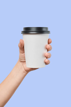 Mockup of men's hand holding white paper mid size cup with black cover isolated on blue background