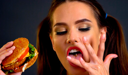 Woman bite big hamburger and lick your fingers after eating. Proper nutrition improves health. Portrait of person with good appetite have greedily dinner. As there is something that you want and do