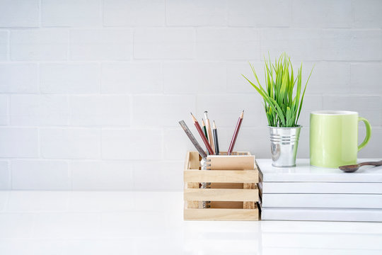 Mock up wooden box of pencil, houseplant and green mug on book on white table with white brick wall