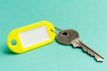 Yellow key tag on a turquoise textured cardboard background.The concept of rent, selling. Template....