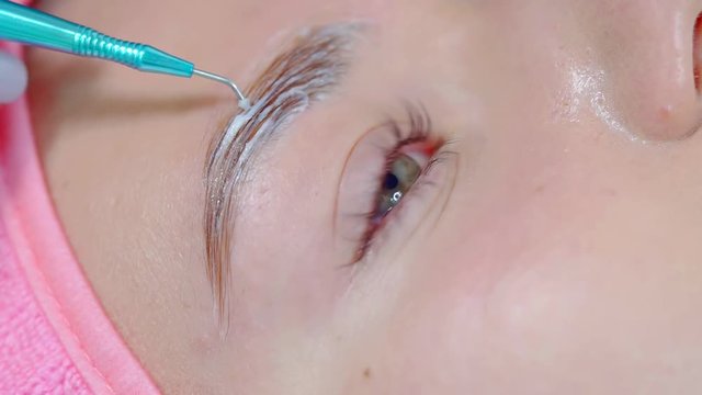 beauty therapist is touching skin and hair of eyebrow during process of coloring brows, close-up in office