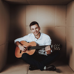 Young Man in Shirt Playing Guitar in Cardboard Box.