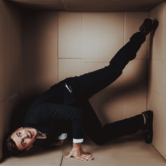 Young Businessman in Black Suit in Cardboard Box.