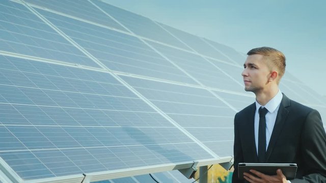 Businessman with a tablet in his hands goes along a row of solar panels. Development of alternative energy. Steadicam shot
