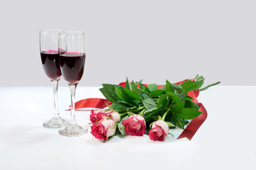 Red roses with red ribbon and two glasses of wine on white and pink background 