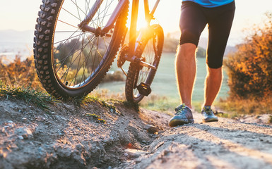 Obraz premium Young cyclist man pushing a mountain bike up the hill close up image. Active adventure travel on bicycle.