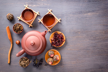 Obraz na płótnie Canvas Several types of green tea, black tea, hibiscus tea and tea ceremony attributes - a ceramic teapot, cups, a strainer, chopsticks and tweezers are placed on an old wooden table. Top view Copy space
