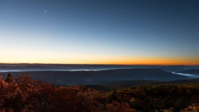 Timelapse, time lapse of Bear rocks overlook in Dolly Sods, West Virginia during dawn, sunrise in autumn, fall with rocky landscape, orange trees, blue sky, yellow sunlight, moon rising, fog