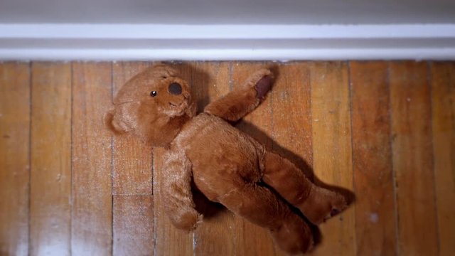 A dramatic bird's eye view of a sad teddy bear being dropped or discarded on a home's hardwood floor.  	