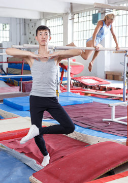 Sporty man asian gymnast during workout in gym,  woman on background
