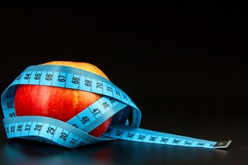 Red apple . Red apple wrapped in a tailor's tape measure on a black background. The concept of weight loss. Healthy diet.