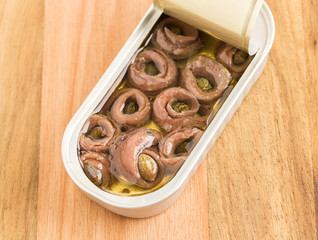 Rolled salty anchovies in open can on wooden background
