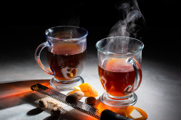 Two Cups of Hot Tea With Orange Peels, Nutmeg and Grater On Marble With Dark Background.
