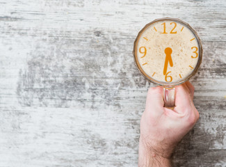 man's hand holds a mug of beer with a silhouette of a clock showing half past six. Concept of alcohol abuse and problems with potency. Top view. Space for text