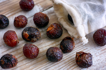Soap nuts spilling from textile bag on wooden background.