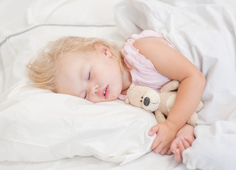 Cute baby girl sleeping on a bed with toy bear