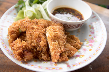 Fried chicken and a cup of sauce and salad on wood table