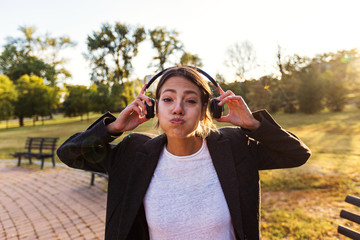 Happy young woman listening music on the headphones in a park