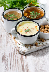assortment of hot soups in mugs on wooden background, vertical top view