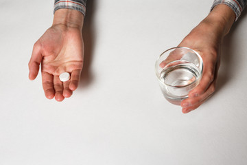 White pill and a glass of water in female hands.