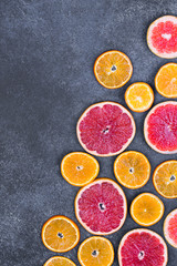 Fresh oranges, grapefruits and madarine slices on dark stone background.