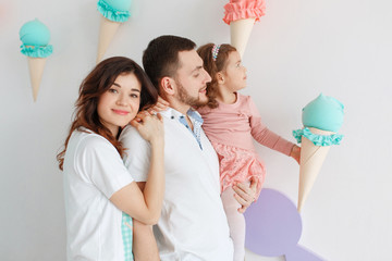 Happy family mother father and daughter standing in studio room with sweet icecream decor