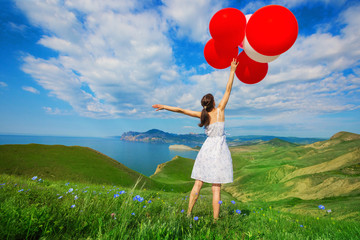 Happy woman with balloons into the field with green grass on the background of beautiful landscape. Celebration on nature outdoors.