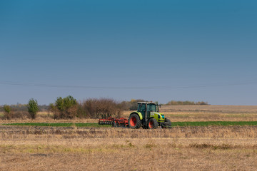 Fototapeta premium Jesienią pole uprawia duży zielony traktor