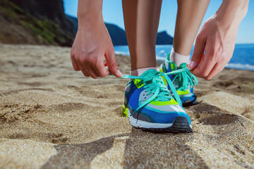 Tying laces on sneakers shoes to jog on the beach. Young woman runner tying shoelaces.