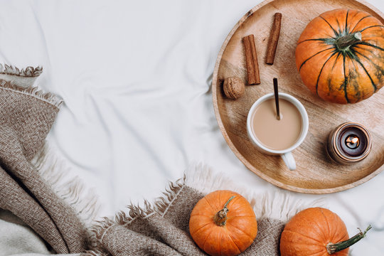 Cozy flatlay with wooden tray, cup of coffee or cocoa, candle, pumpkins on white sheets and blankets