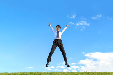 Fototapeta na wymiar 青空をバックにバンザイしながらジャンプするYシャツ姿の若いビジネスマン1人。成功・達成・成就・元気・健康イメージ