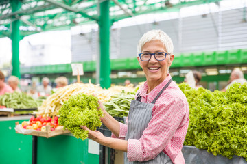Senior woman sells lettuce on marketplace