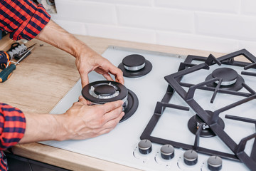 Close up of man hand install burner ongas hob in kithen. Repairs of gas control panel