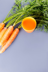 Carrot juice and carrots close up on a grey wooden background.