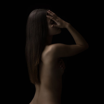 Healthy spine and hair of young woman on black background, covering her face with hand. Low key