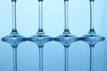 Row of glass cups stems. Reflective surface, blue lighting.