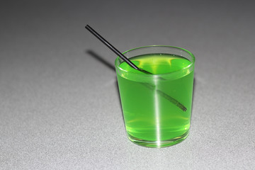 a green drink in a transparent glass with a black straw on a gray table
