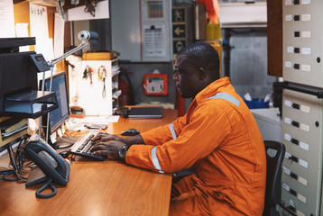 African marine engineer officer in engine control room ECR. Seamen's work. He works at the computer