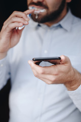 close up of man using smartphone. concept of phone addiction. young business man typing and browsing social media on his phone while brushing his teeth. 