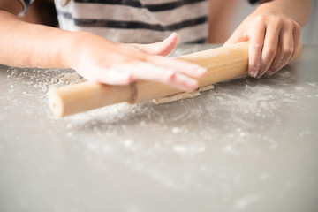 the child rolls with a rolling pin dough, cooks food on the gray desktop with the scattered flour