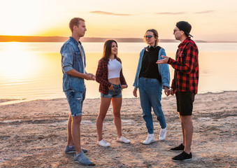 Group of modern couples on beach together walking during sunset. They talk, laugh and have fun