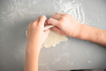 the child rolls with a rolling pin dough, cooks food on the gray desktop with the scattered flour