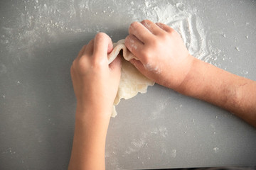 the child rolls with a rolling pin dough, cooks food on the gray desktop with the scattered flour