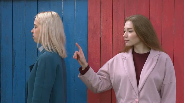 Girls on colourful eco wooden background.
Relationships between girls. Girl on the right turns toward girl on the left and touches her by finger in order to attract her attention.