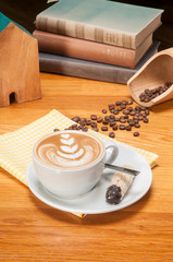 Cup of coffee latte and coffee beans with books on wooden table