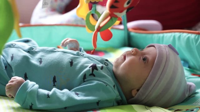 baby boy lies on a developing rug and looks at the toys that hang on top